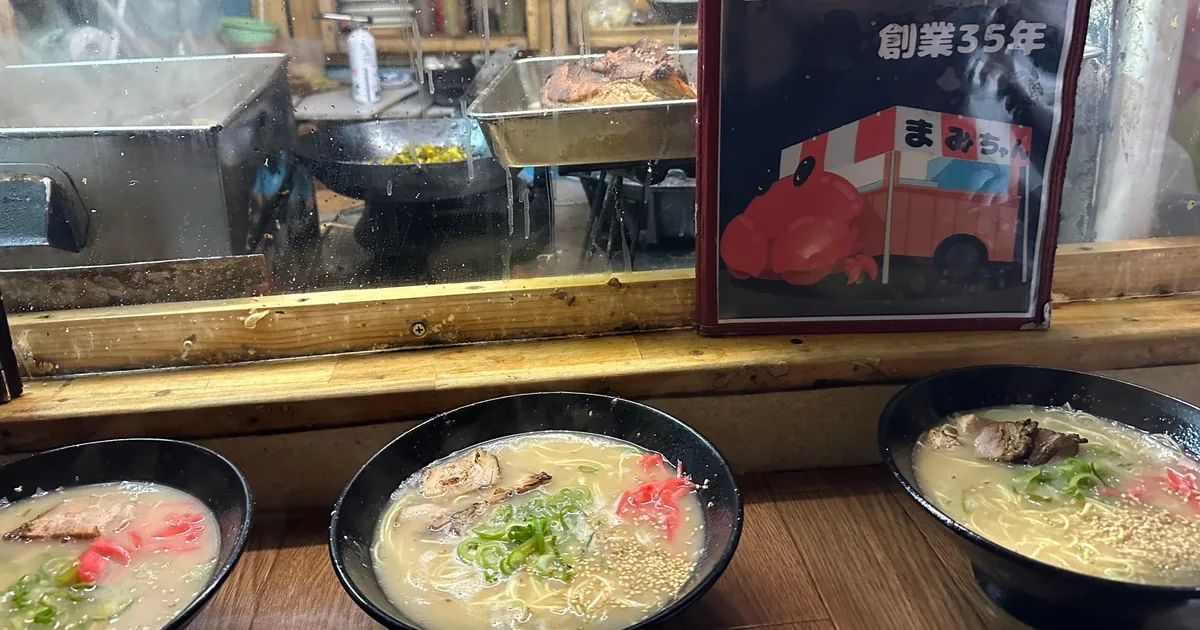 屋台のカウンターに並ぶ、クリーミーな豚骨ラーメン3杯